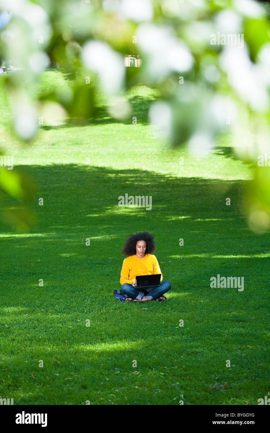 Giovane uomo con capelli afro seduto sull'erba con il computer portatile Foto Stock