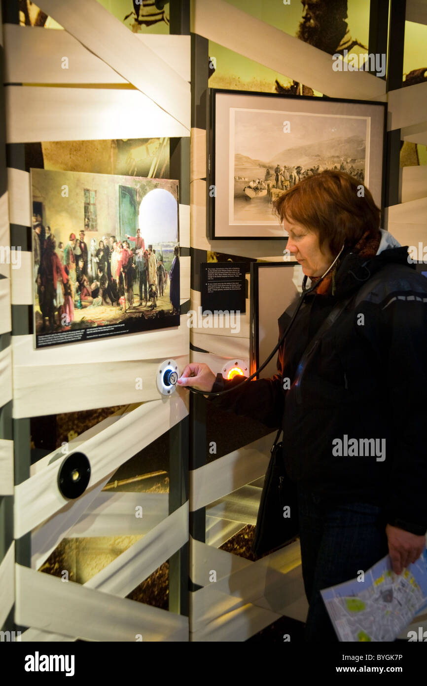 Tourist indossando 'stethoscope' le cuffie / cuffie audio guida guardando un display. Florence Nightingale Museum. Londra. Regno Unito. Foto Stock