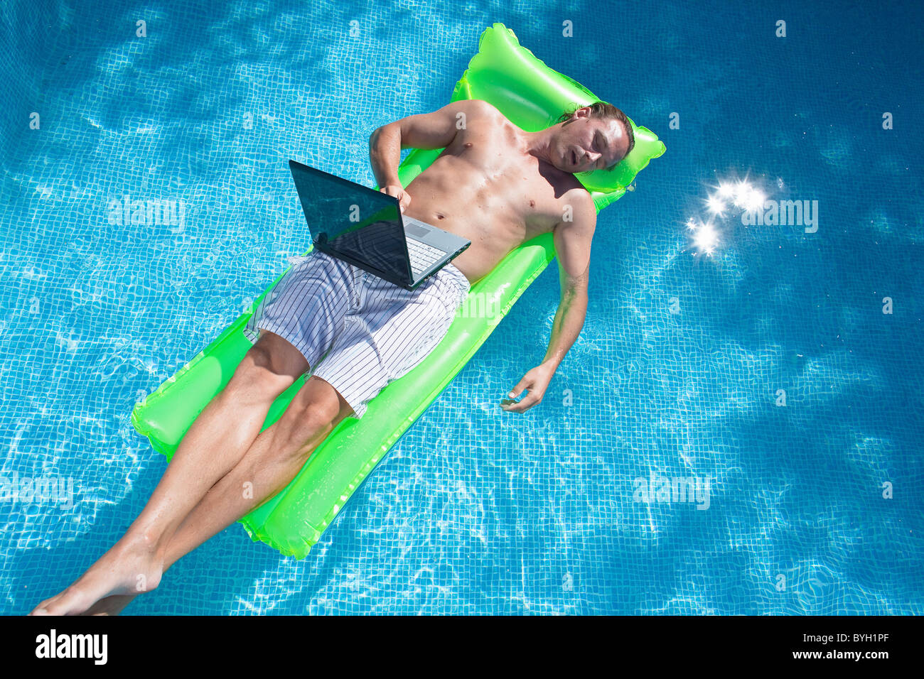 L'uomo galleggiante sulla zattera gonfiabile con il computer portatile e il sonno Foto Stock