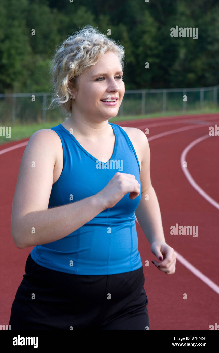 Una giovane donna che è un po' sovrappeso corre la via per bruciare calorie. Foto Stock