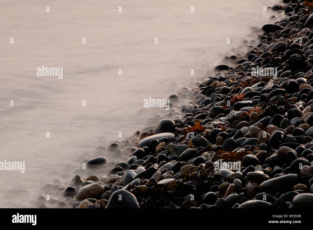 Ciottoli e onde nebuloso, Cemlyn Bay Foto Stock