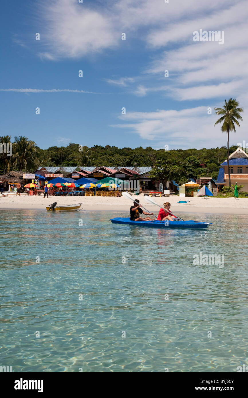 Fotografia di una costa con due persone canoa mentre una barca negozi ombrelloni e una foresta sono evidenti in background Foto Stock