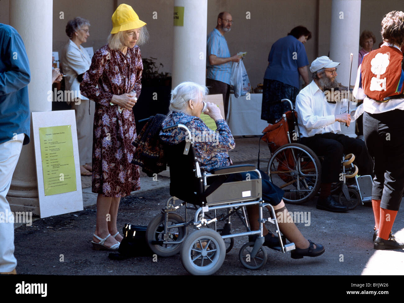 Due donne anziane prendendo tè nel parco con uno in una sedia a rotelle e altri assistere Foto Stock