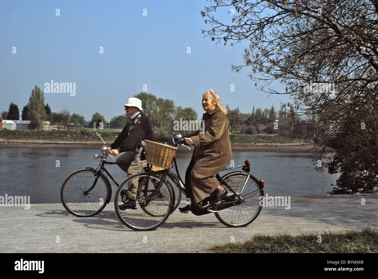 Due persone anziane in bicicletta lungo il lato di un fiume Foto Stock
