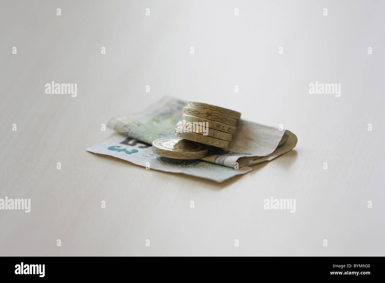 Alcuni sterling £1 monete in appoggio su un piegato £5 nota Foto Stock