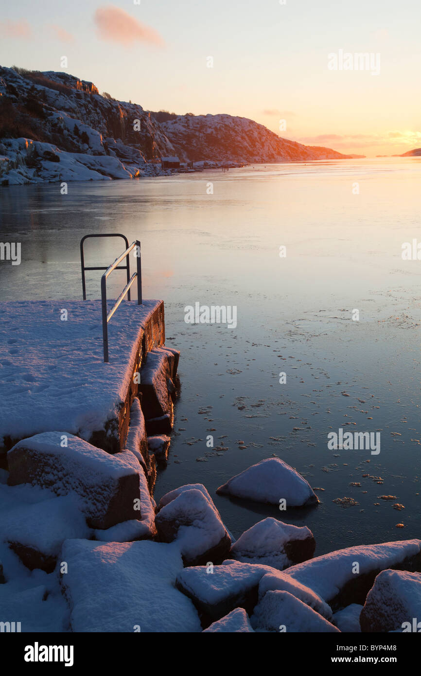 Una coperta di neve jetty, e mare ghiacciato al tramonto Foto Stock