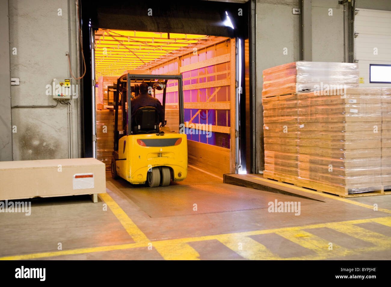 Operatore carrello elevatore a forche di carico pallet avvolto di scatole di cartone sul rimorchio in magazzino Foto Stock