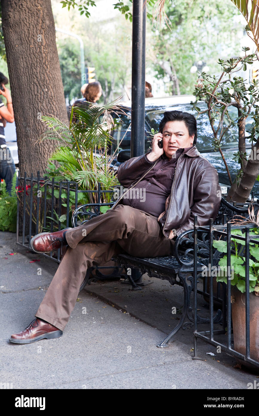 Giovani paunchy Diego Rivera si assomigliano seduta su ghisa panchina al di fuori cafe su Avenida Alvaro Obregon parlando sul suo cellulare Foto Stock
