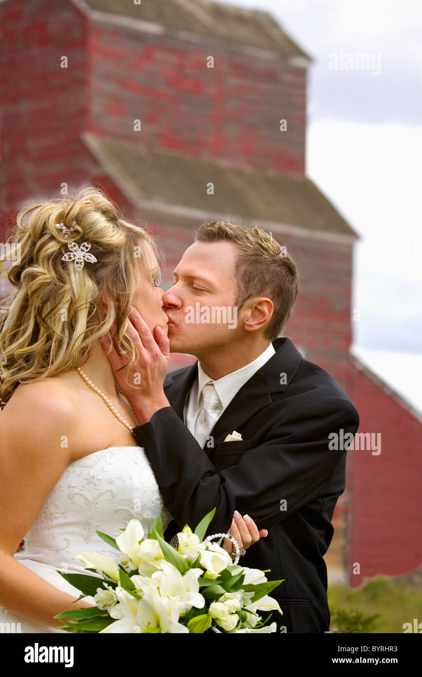 Lo sposo abbracciando la sua sposa come egli bacia il davanti di un vecchio paese di elevatore della granella; st. Albert, Alberta, Canada Foto Stock