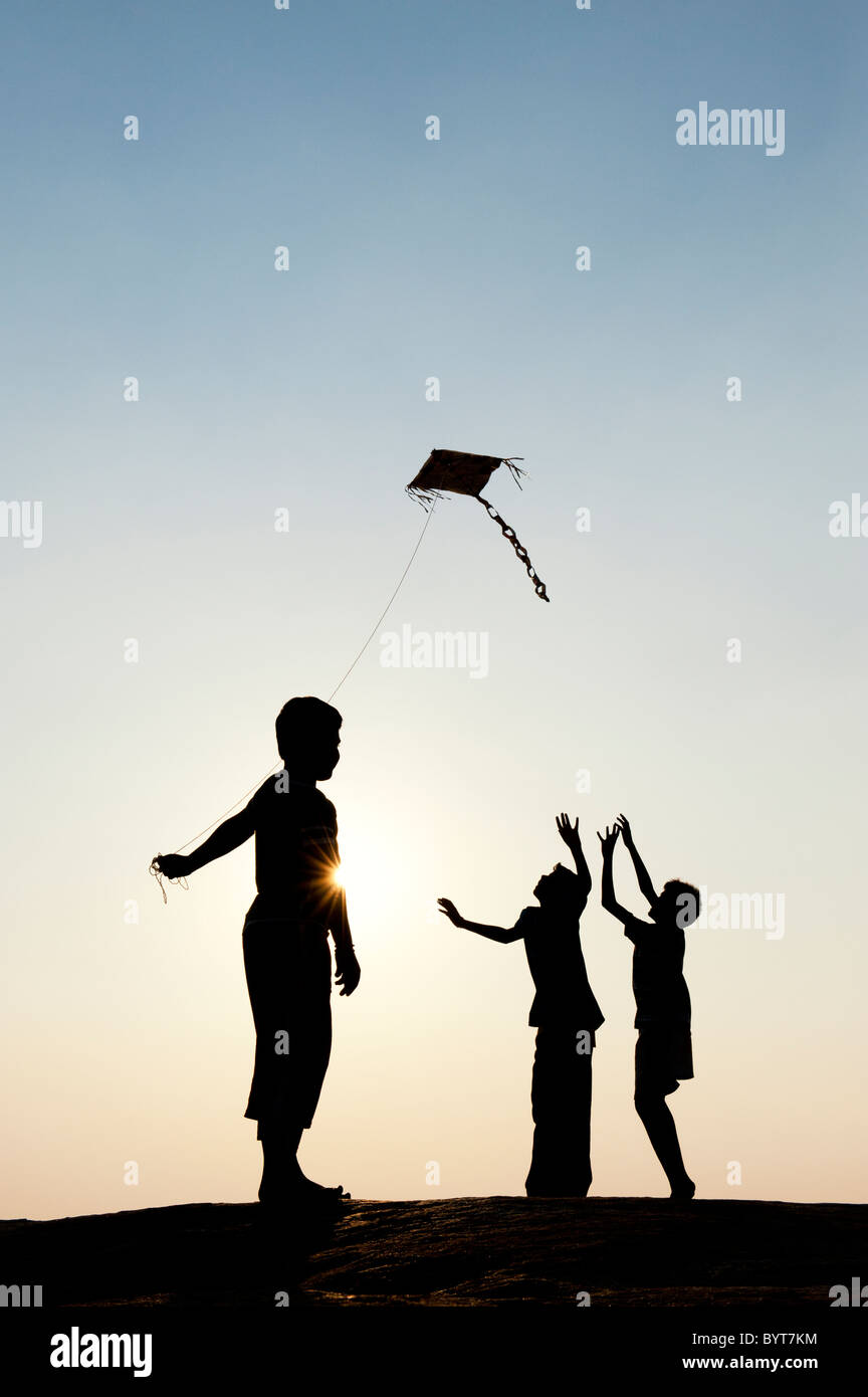 Giovani indiani ragazzi divertirsi battenti una carta fatta a mano il kite in campagna indiana. Silhouette Foto Stock