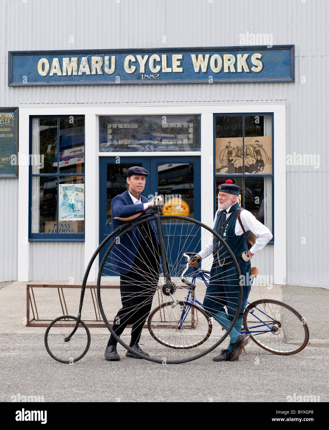 Due ciclisti in costume con un Penny Farthing noleggio al di fuori di un negozio di biciclette a Oamaru, Nuova Zelanda Foto Stock