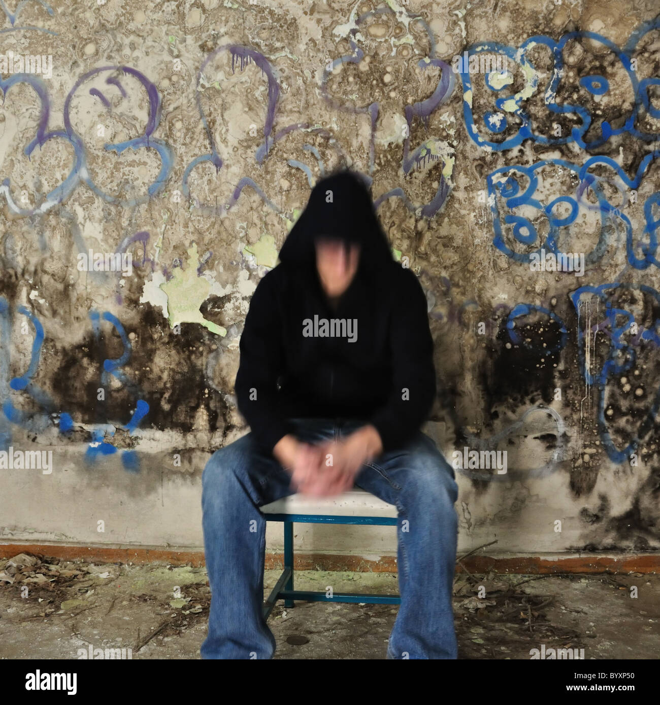Sfocata figura maschile seduto contro il muro sporco ricoperta di muffa nera e vernice disordinato. Foto Stock
