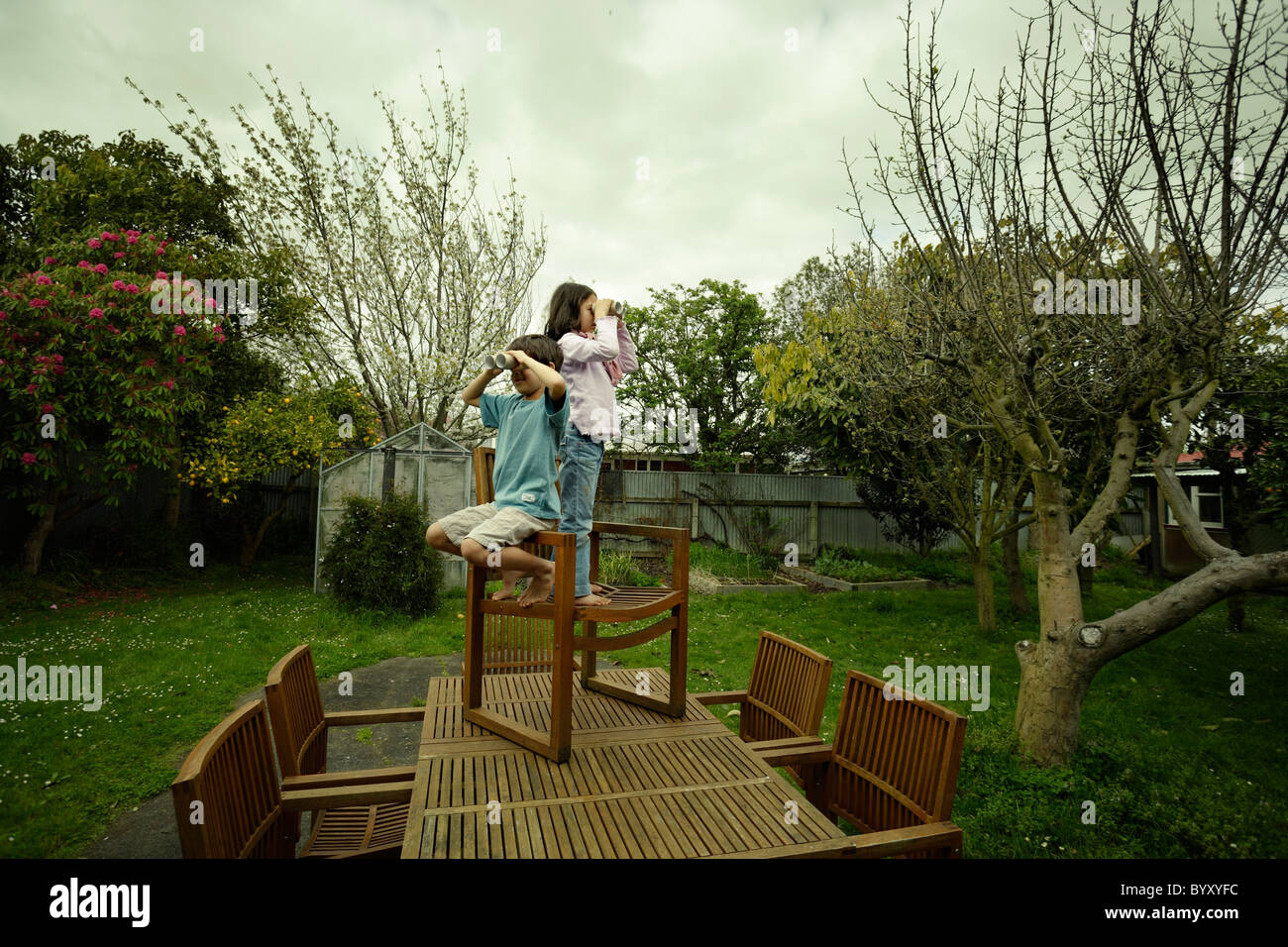 Un ragazzo e una ragazza riposare su una sedia sul tavolo da giardino, utilizzando tubi di cartone come fingere binocolo. Foto Stock