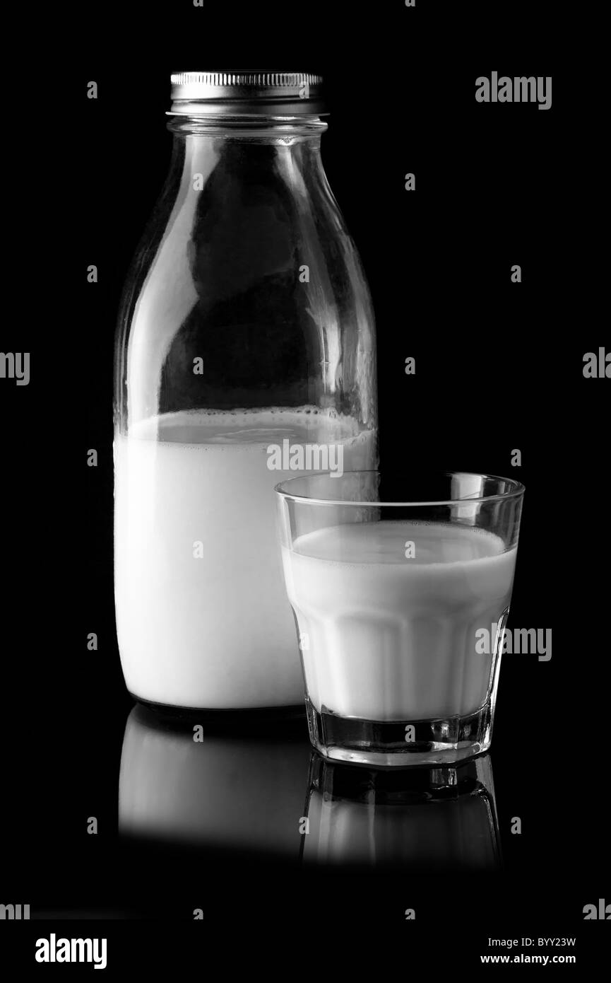 Un bicchiere di latte e bottiglia su sfondo nero. Bianco e Nero immagine Foto Stock
