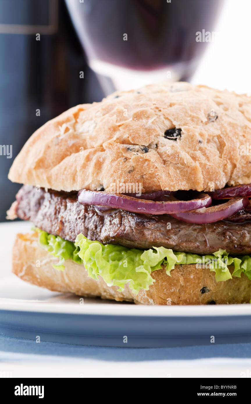 Hamburger di manzo con bistecca di manzo e anelli di cipolla e vino rosso come primo piano su uno sfondo bianco Foto Stock