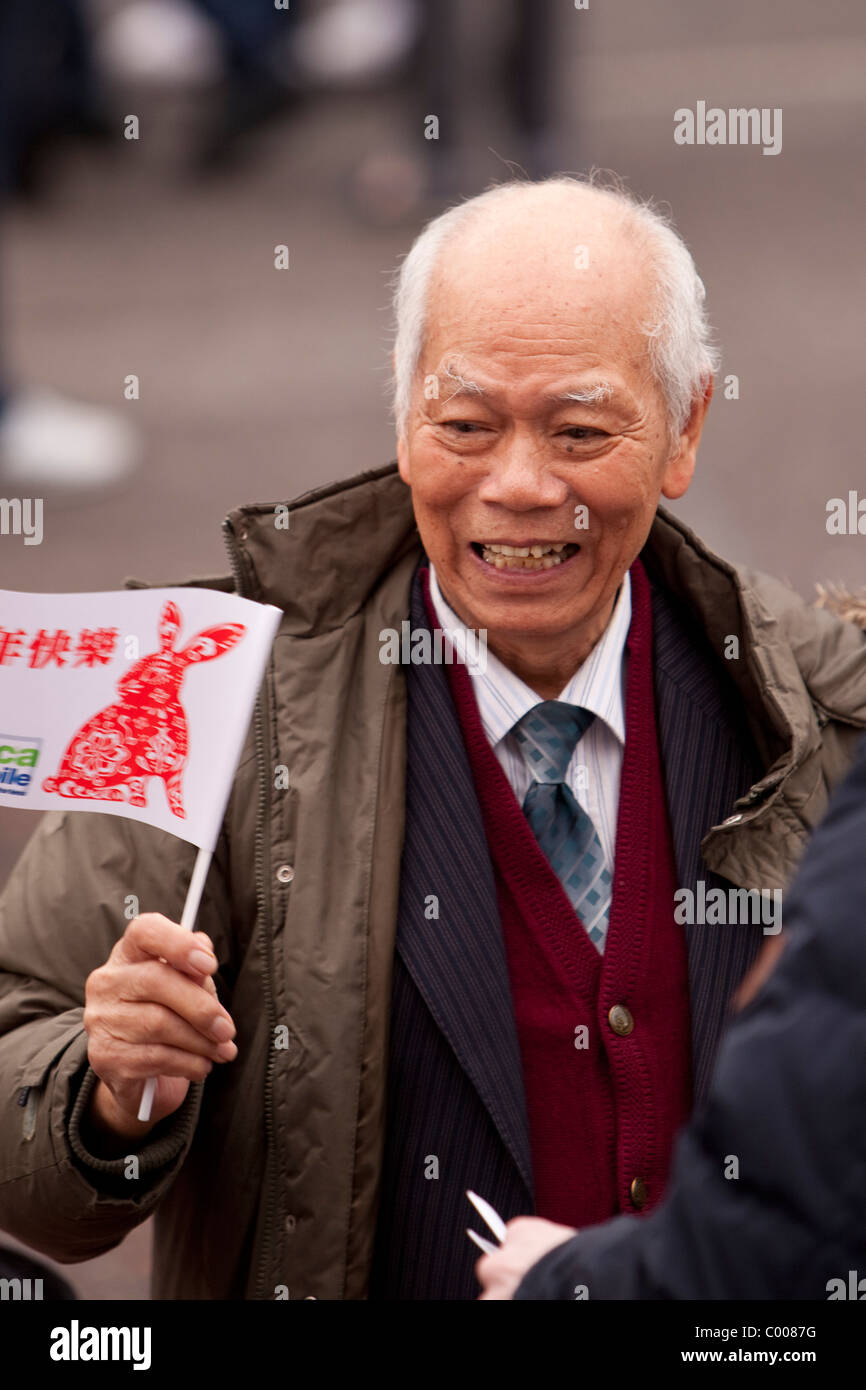 Un anziano gentiluomo sventola una bandiera fortunato durante il Capodanno cinese Foto Stock