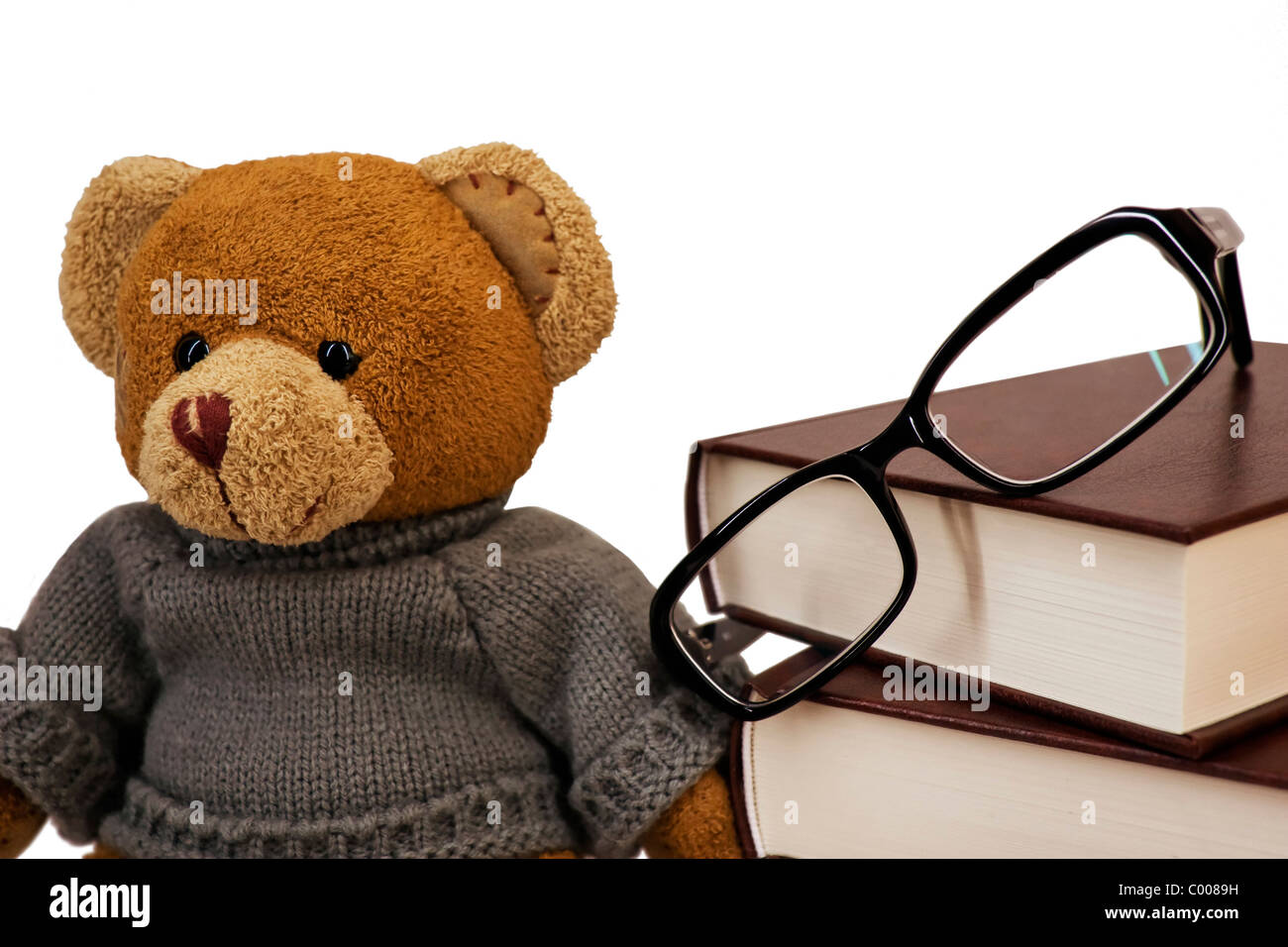 Orsacchiotto di peluche, bicchieri e una pila di vecchi libri su sfondo bianco Foto Stock