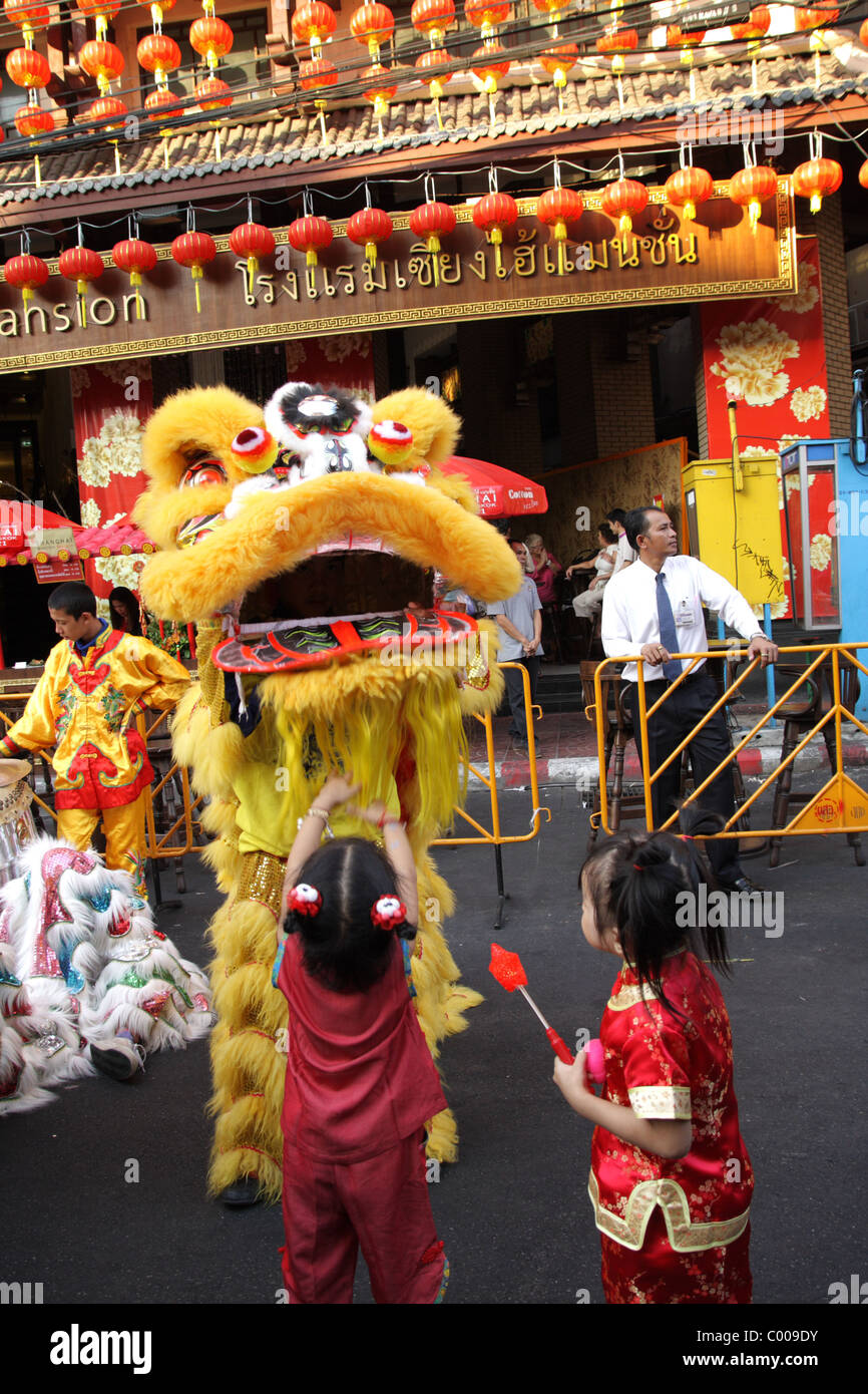 Bambini che giocano con il cinese la danza del leone di esecutori festeggiare il nuovo anno cinese in una strada a Bangkok Foto Stock