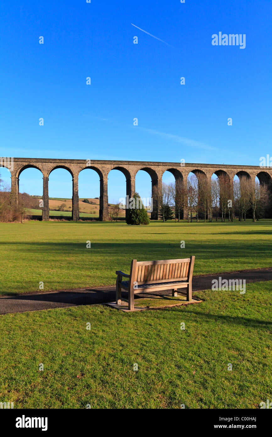 Panca in legno in acqua prati Park rivolta verso il viadotto ferroviario, Penistone, South Yorkshire, Inghilterra, Regno Unito. Foto Stock