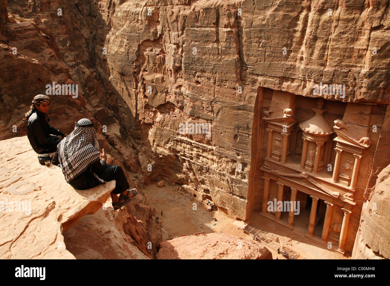 I beduini seduto sulla cima di una scogliera guardando giù al tesoro (El Khazneh), Petra, Giordania. Foto Stock