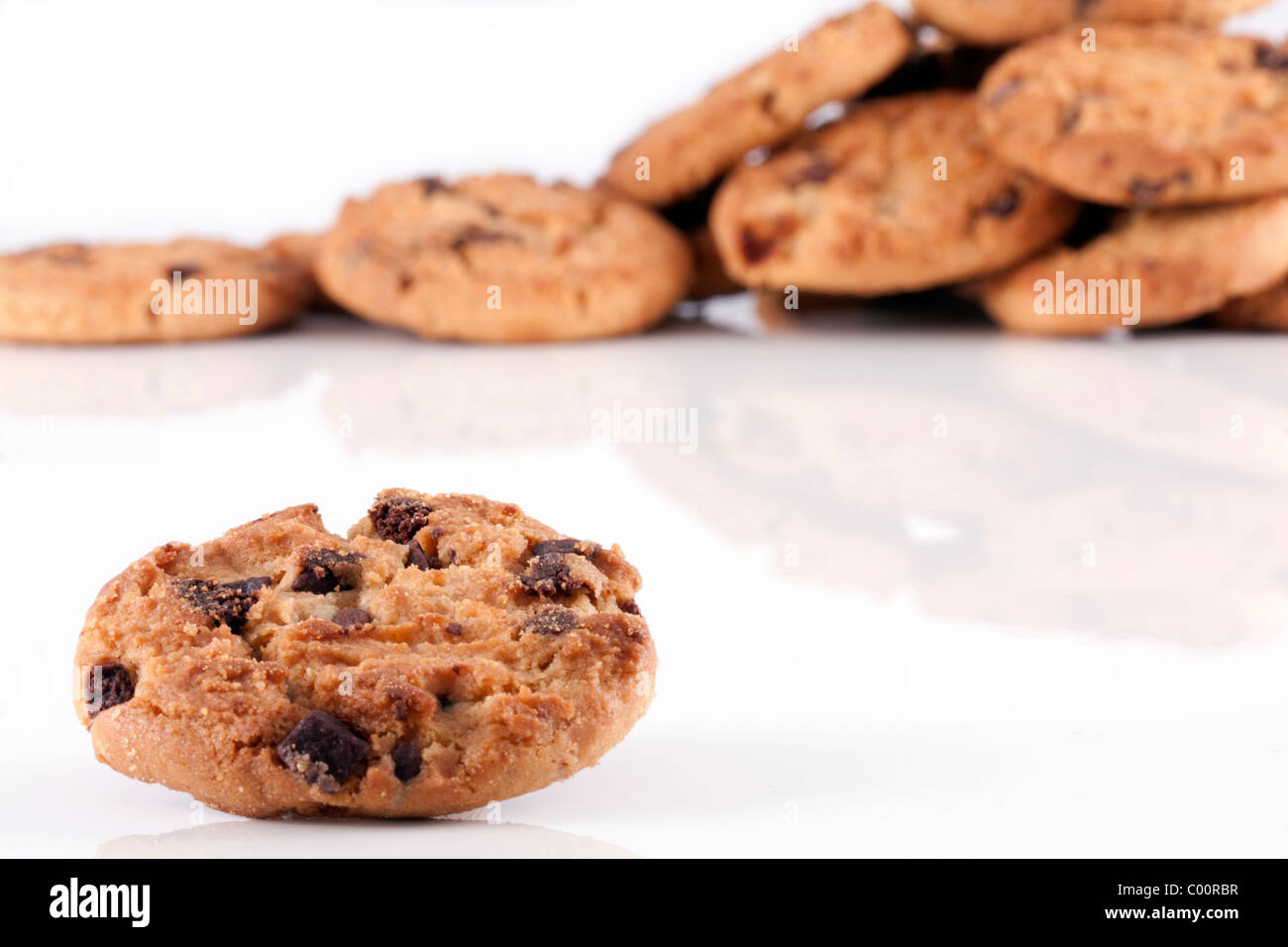 Close up di un Chocolate Chip Cookie con una pila di biscotti al cioccolato unsharp in background sul bianco. Foto Stock