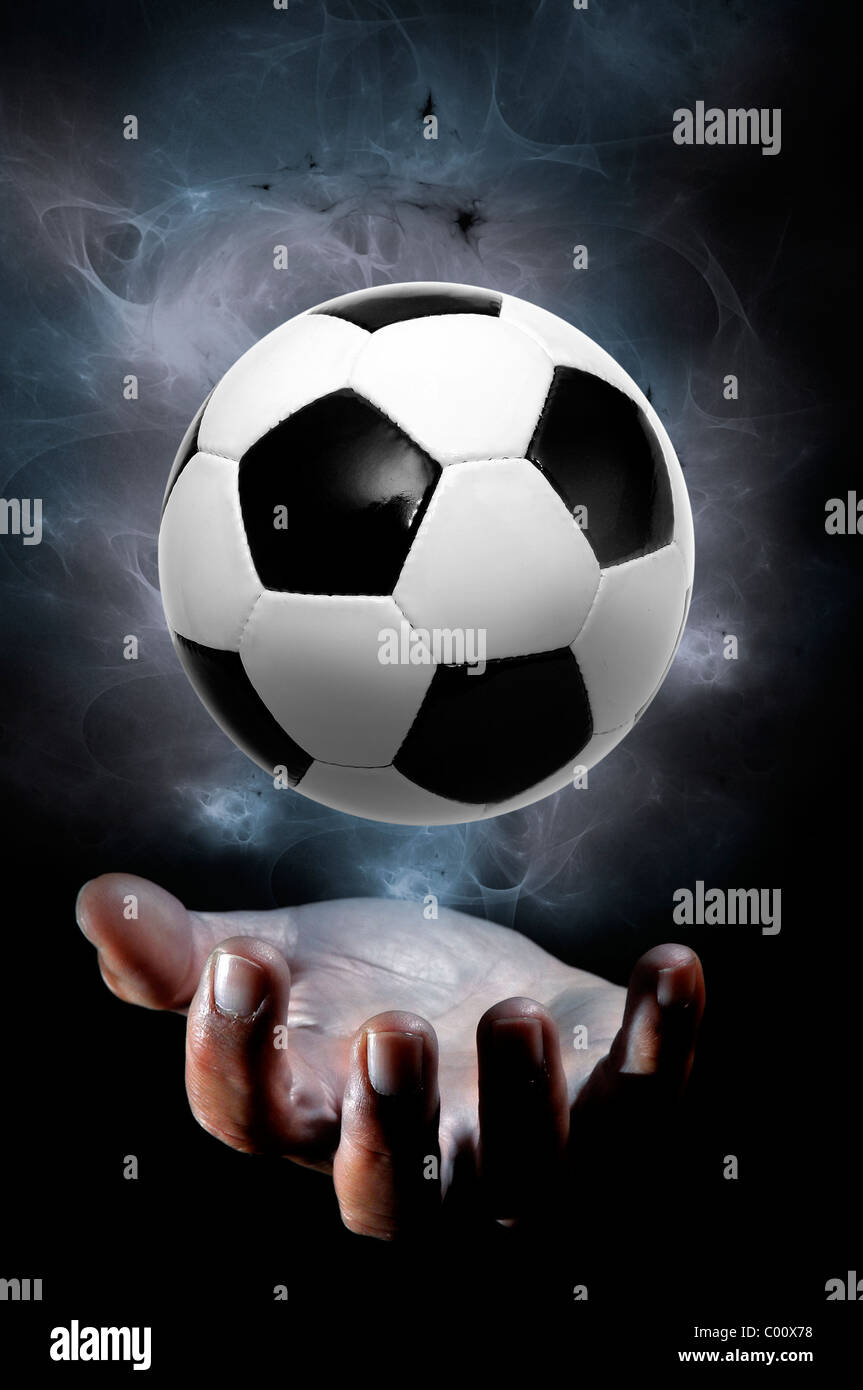 Mano umana con un pallone da calcio isolato in uno sfondo nero Foto Stock
