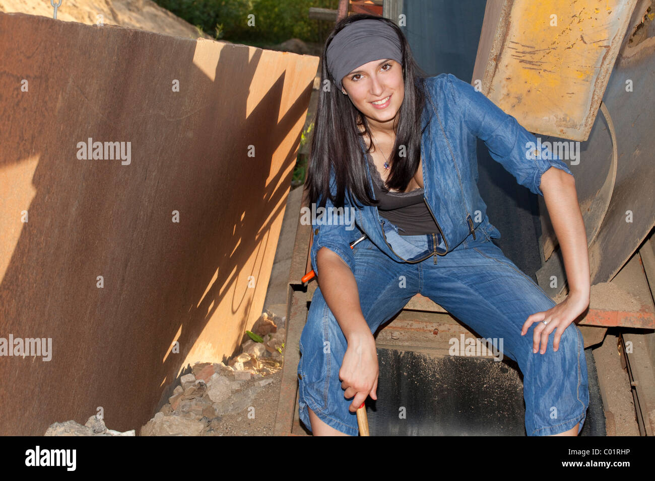 Giovane donna indossa una tuta in jeans di fronte macchine industriali Foto Stock