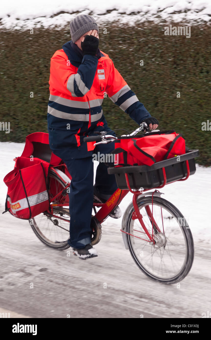 Un Royal Mail portalettere che mostra il movimento in bicicletta sul suo giro nella neve nel Regno Unito Foto Stock