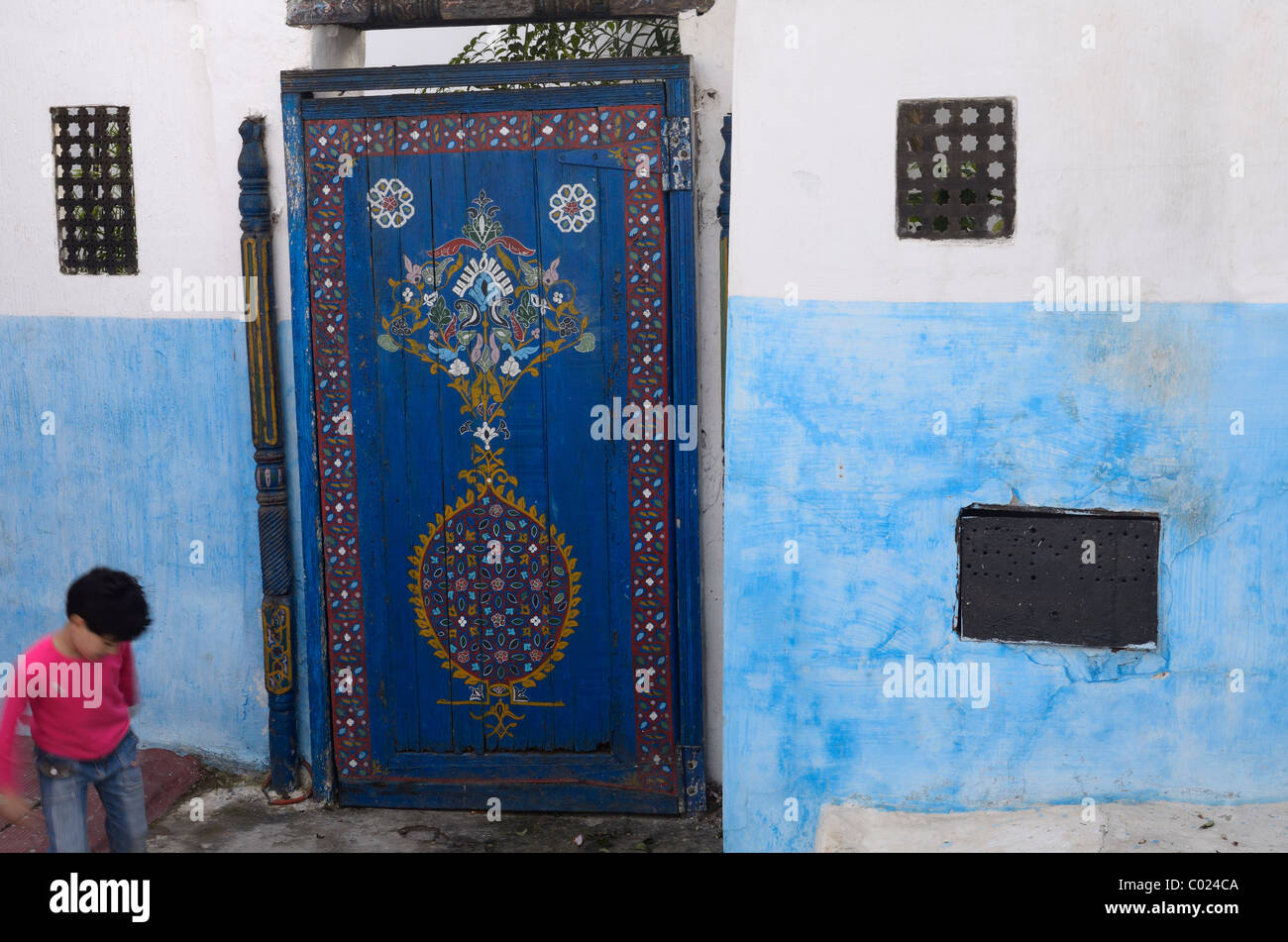 Ragazza che gioca accanto al dipinto di blu porta in un vicolo di Oudaia Kasbah Marocco Rabat Foto Stock