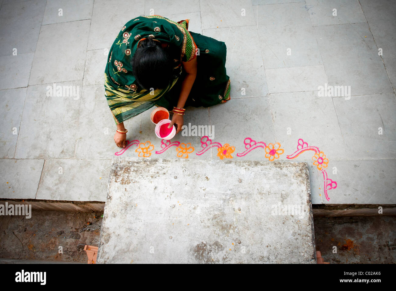 Una donna indiana dipinge un motivo floreale sul terreno su Bhopal in India. Foto Stock