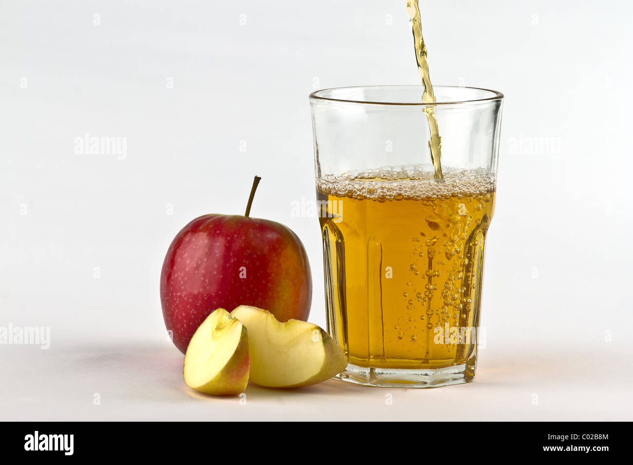 Sidro di mela versando in giù in vetro con le mele a lato. Su sfondo bianco Foto Stock