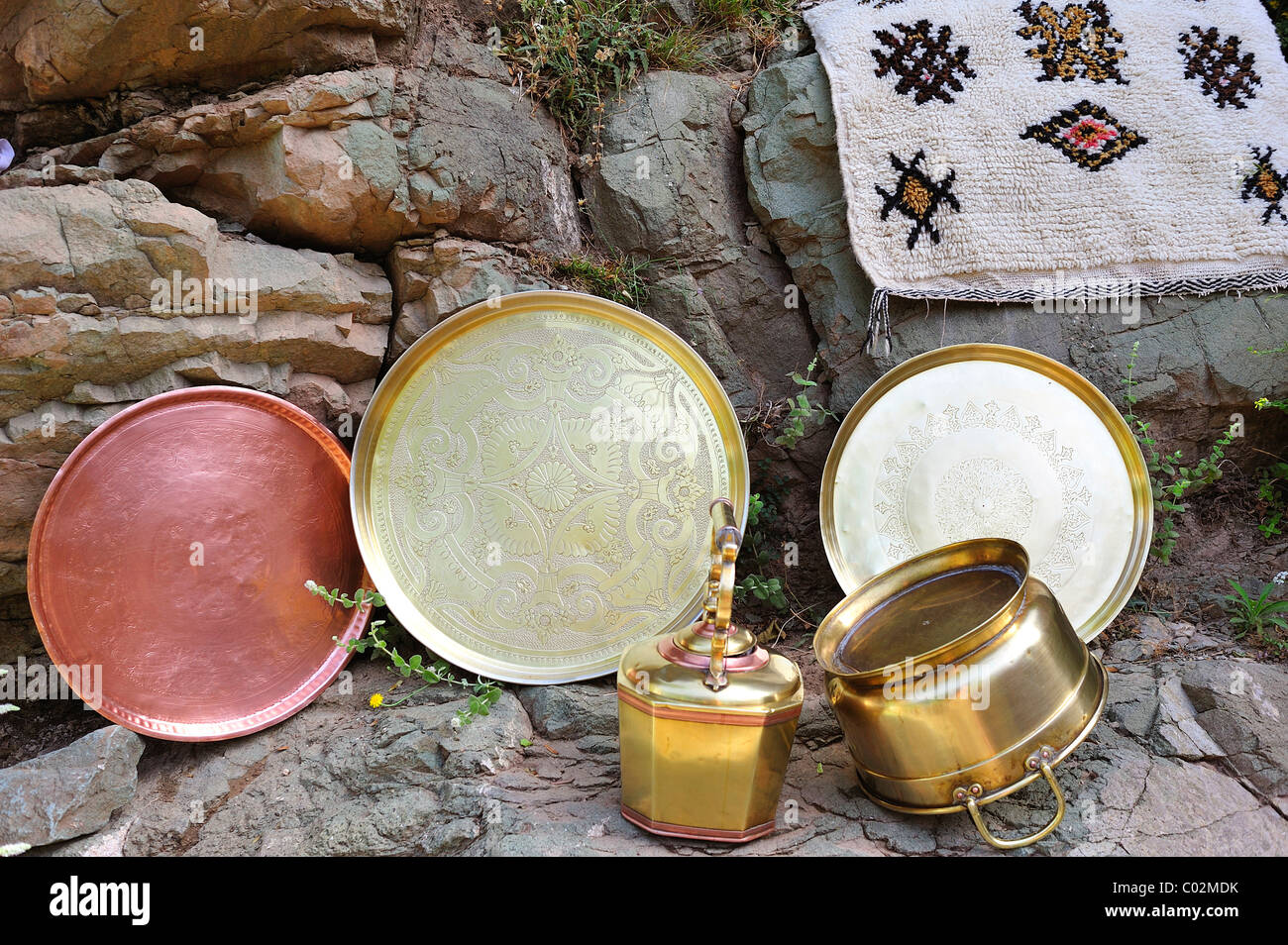 Lavate riccamente Ottone inciso vassoi e pentole disposte su una roccia a secco, Alto Atlante, Marocco, Africa Foto Stock