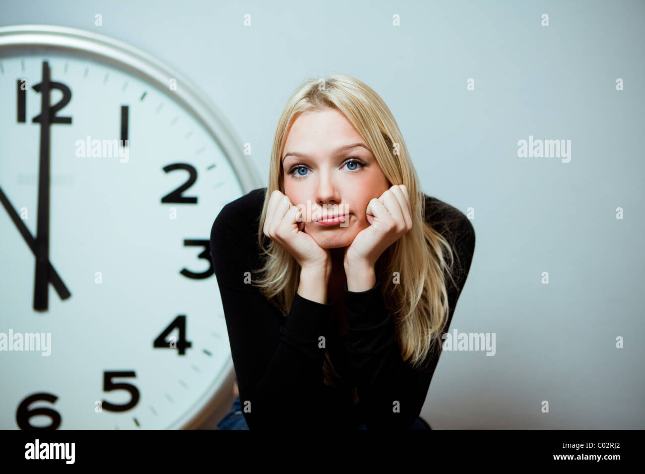 Annoiato donna con un grande orologio da parete Foto Stock