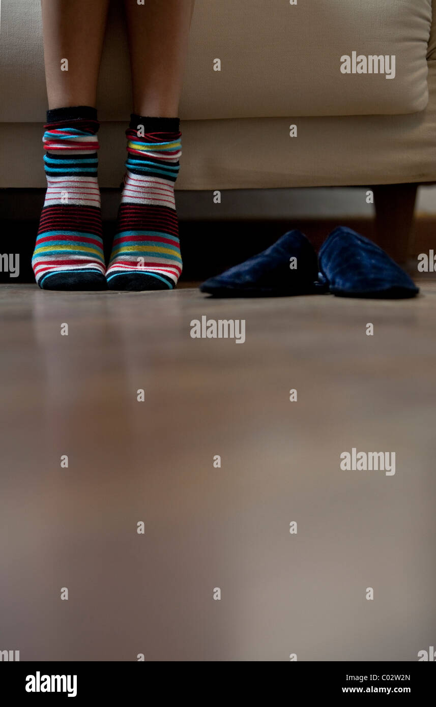 I piedi di una donna seduta su un divano con calze colorate Foto Stock
