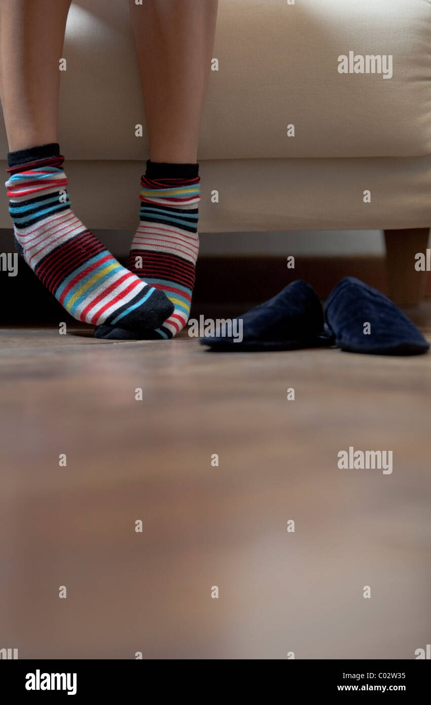 I piedi di una donna seduta su un divano con calze colorate Foto Stock