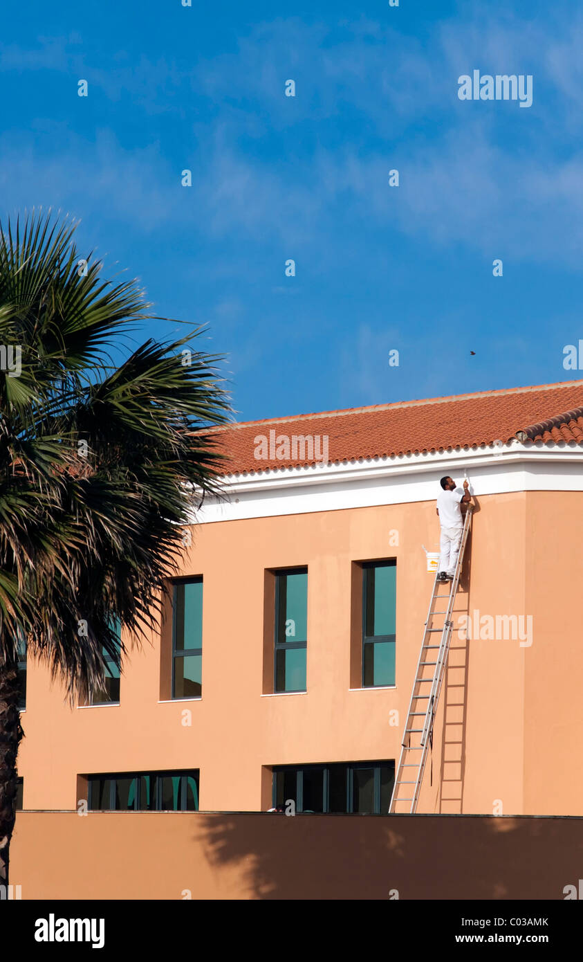 Pittore su un alta scala appoggiata sulla facciata di un hotel per le vacanze, Novo Sancti Petri, Andalusia, Spagna, Europa Foto Stock