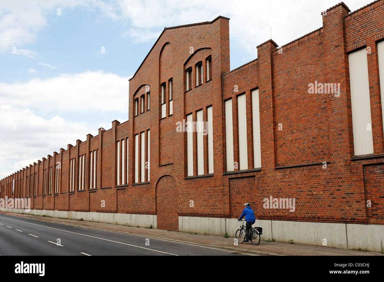 Ciclista passato di equitazione la facciata in mattoni di una ex fabbrica, Batteriestrasse, porto industriale di Neuss, Niederrhein Foto Stock
