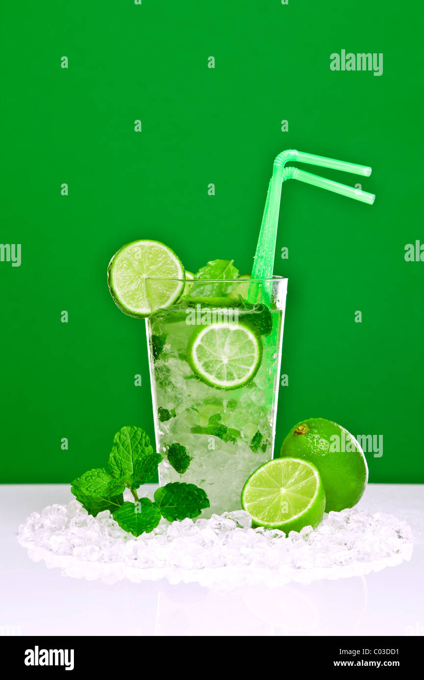 Foto di un cocktail mojito con fresco di lime e foglie di menta su una barra bianca con sfondo verde. Foto Stock