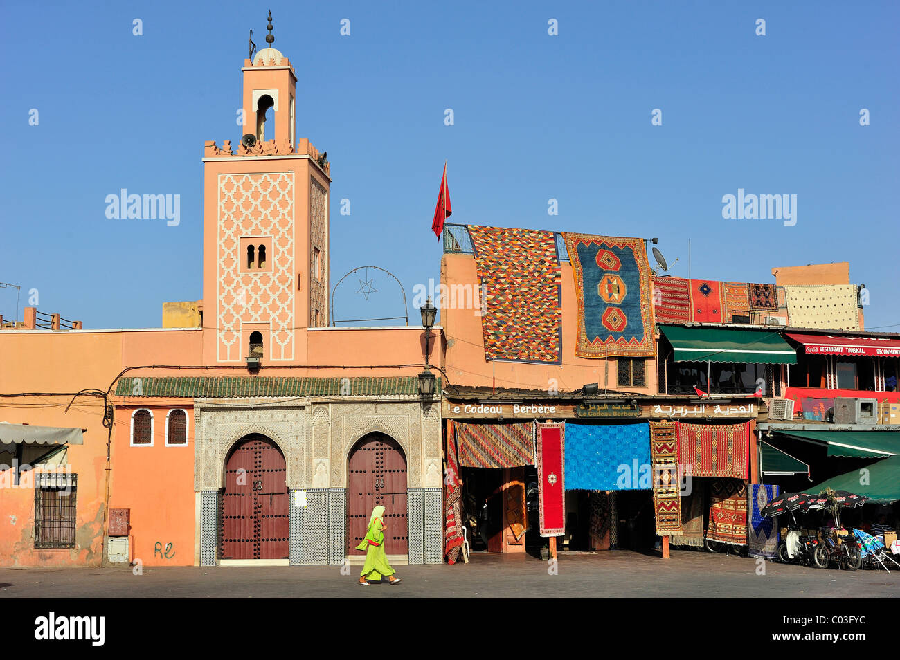 Moschea con un minareto, accanto a un tappeto il concessionario vende tappeti, Djemaa el Fna, il gruppo dei morti a Marrakech, Marocco, Africa Foto Stock