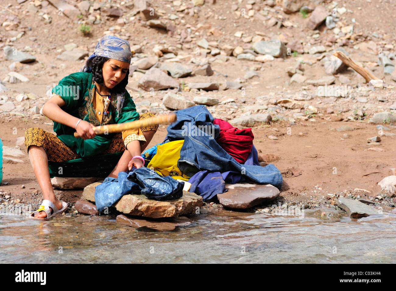 Giovane donna che indossa un velo il lavaggio della biancheria con un bastone su un argine, Alto Atlante, Marocco, Africa Foto Stock