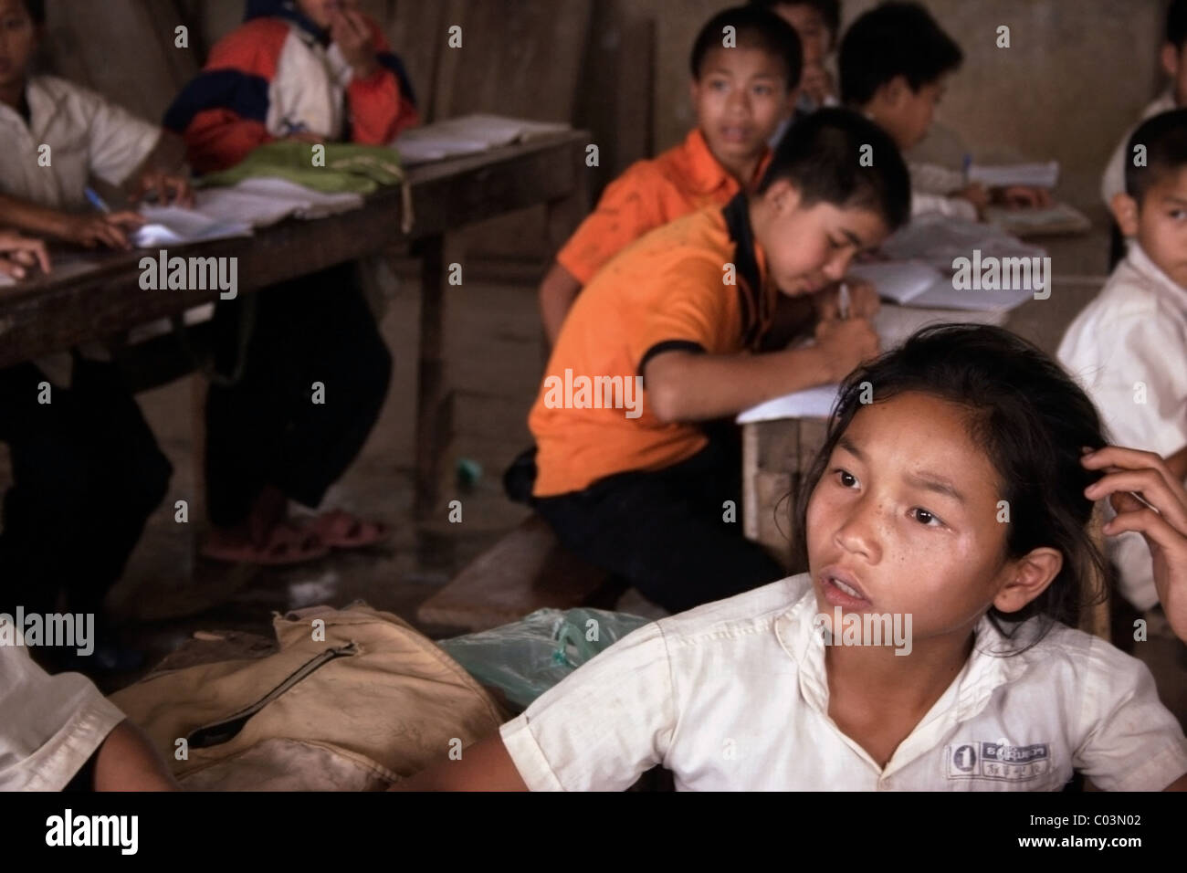 Una ragazza giovane studente sembra essere il pensiero guardando fuori una finestra in corrispondenza di una fatiscente scuola primaria nelle zone rurali del Laos comunista. Foto Stock