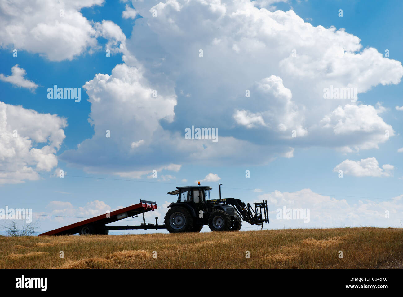 Trattore agricolo e il rimorchio in campo secco sotto nuvoloso cielo blu Foto Stock