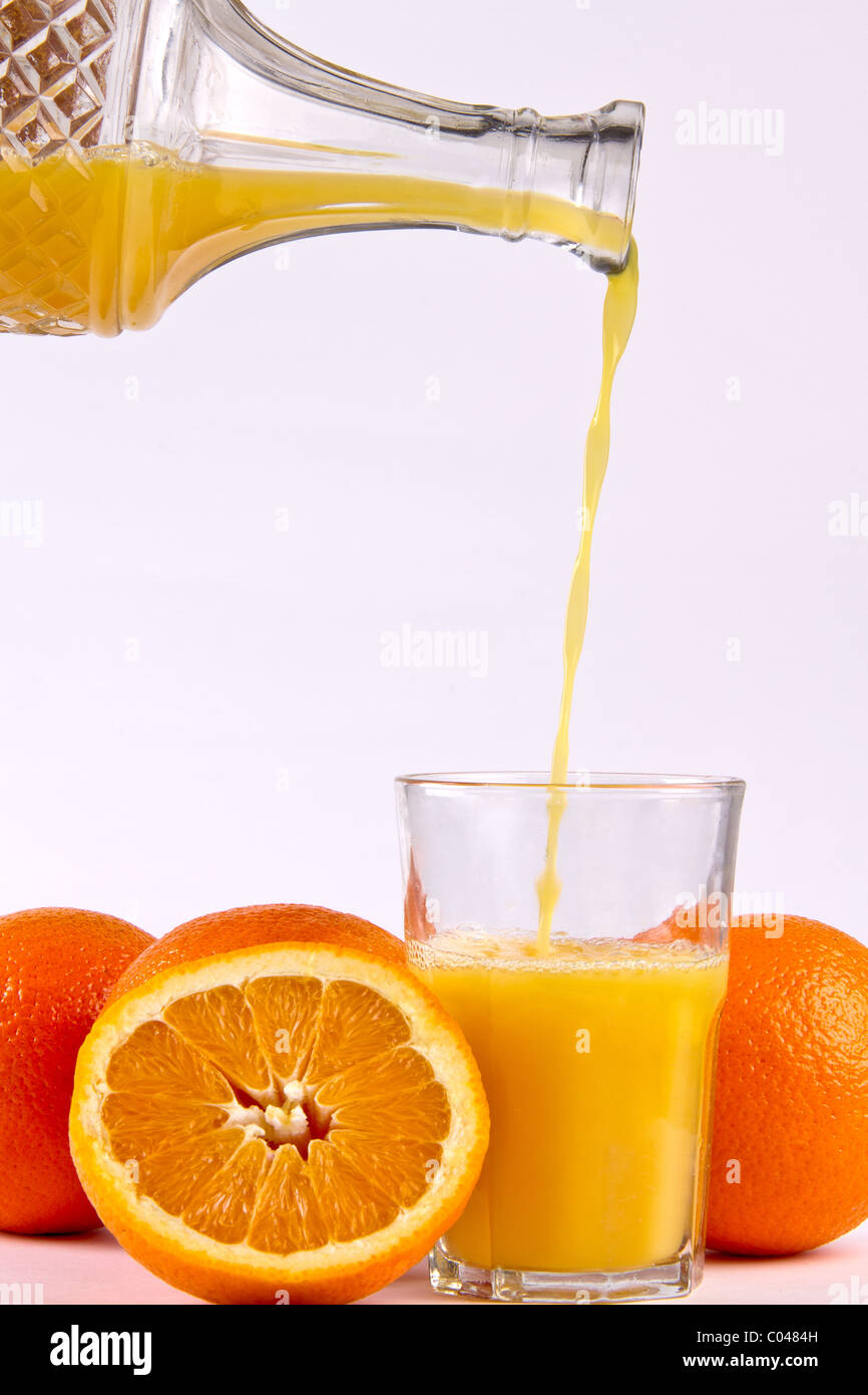 Succo di arancia che viene versato in un bicchiere circondato da frutti di colore arancione Foto Stock