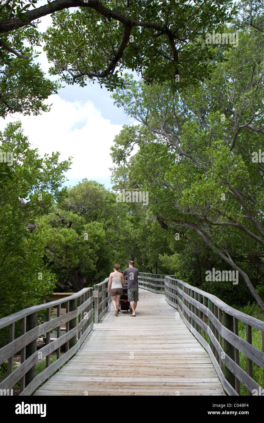 Una giovane coppia spingere un passeggino lungo un rilievo passerella in legno in un preservare la zona di Anne's Beach in Florida Keys. Foto Stock