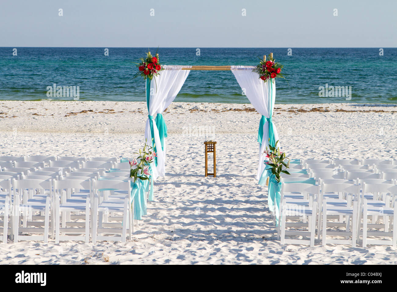 Wedding archway, sedie e i fiori sono disposti sulla sabbia in preparazione per una spiaggia di cerimonia nuziale. Foto Stock