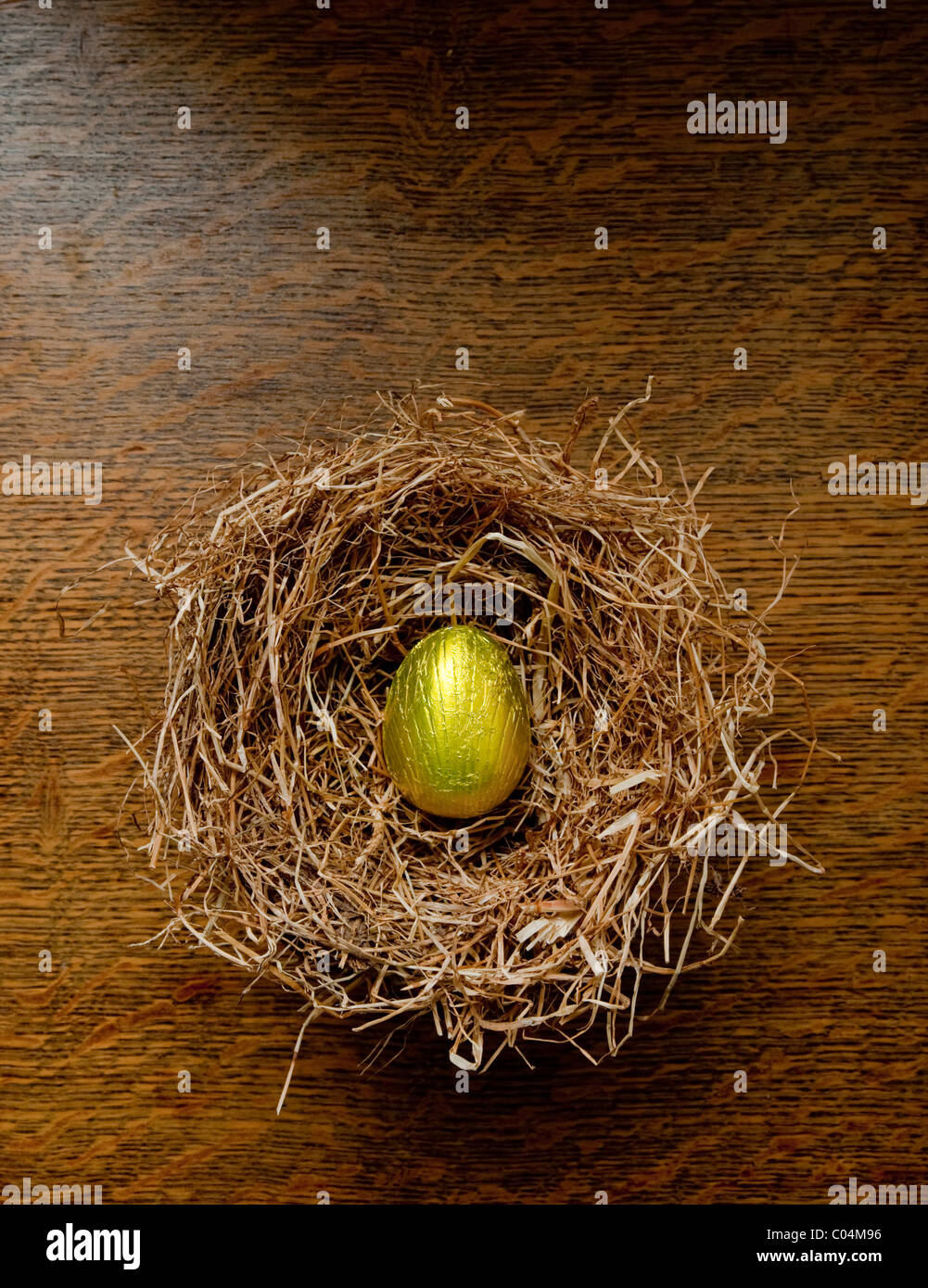 Singola lamina oro avvolto di cioccolato uovo di pasqua in un fieno di nidificazione degli uccelli su un tavolo in legno di quercia. Foto Stock