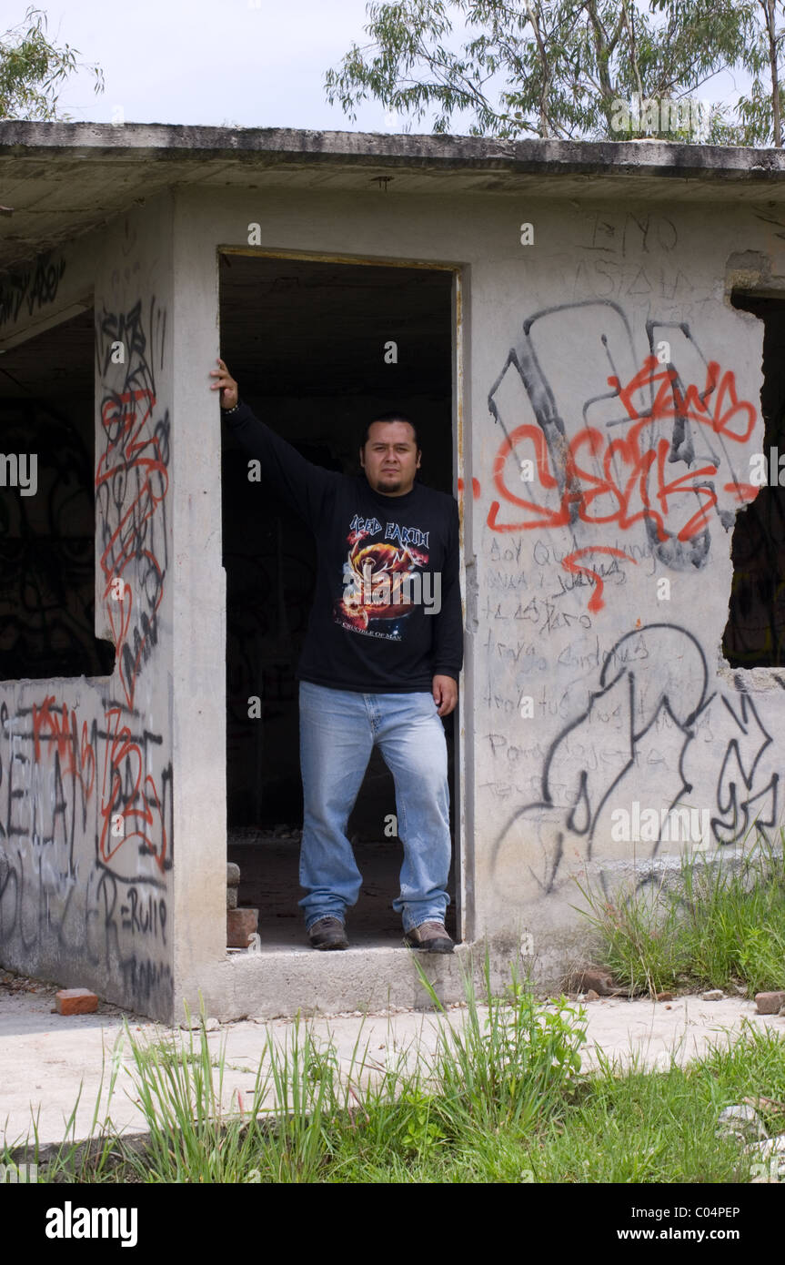 Uomo messicano di indossare una maglia a manica lunga t-shirt all'interno di una costruzione abbandonata piena di graffiti Foto Stock