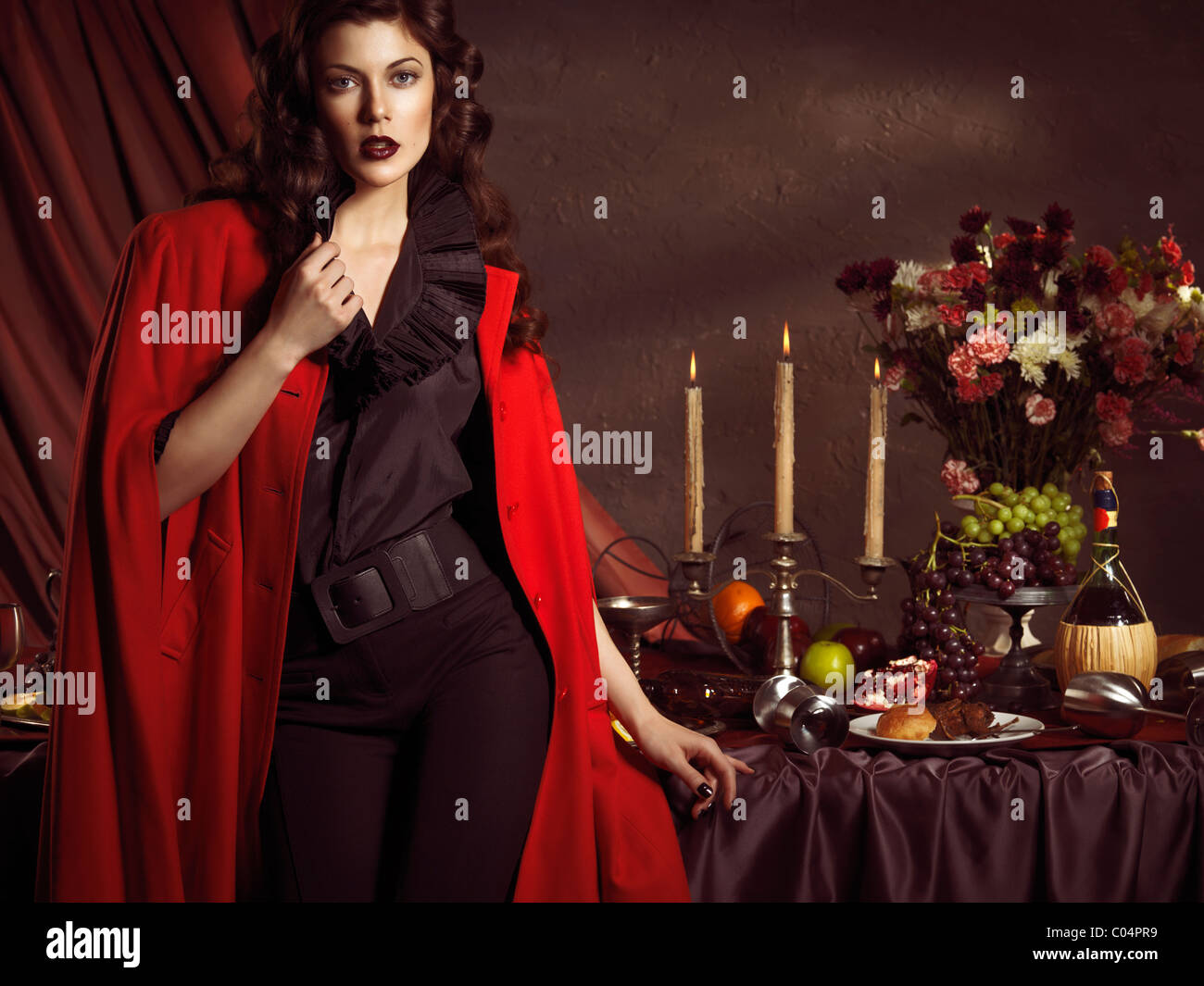 Licenza e stampe a MaximImages.com - Foto di alta moda di una bella donna in cappotto rosso in piedi a un tavolo con i resti di una cena di festa Foto Stock