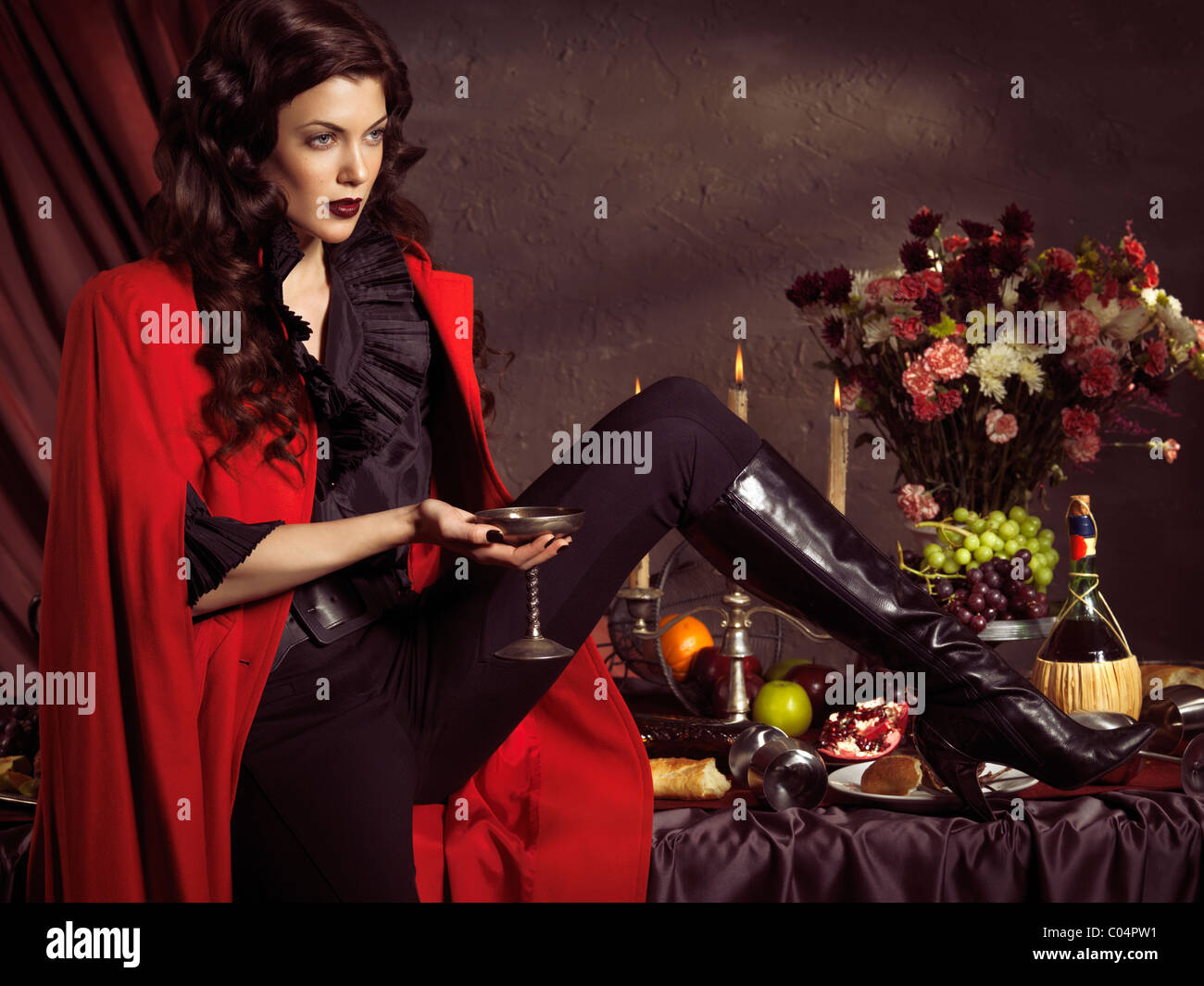 Licenza e stampe a MaximImages.com - Foto di alta moda di una bella donna in cappotto rosso seduto su un tavolo festivo con un bicchiere di vino nel suo han Foto Stock
