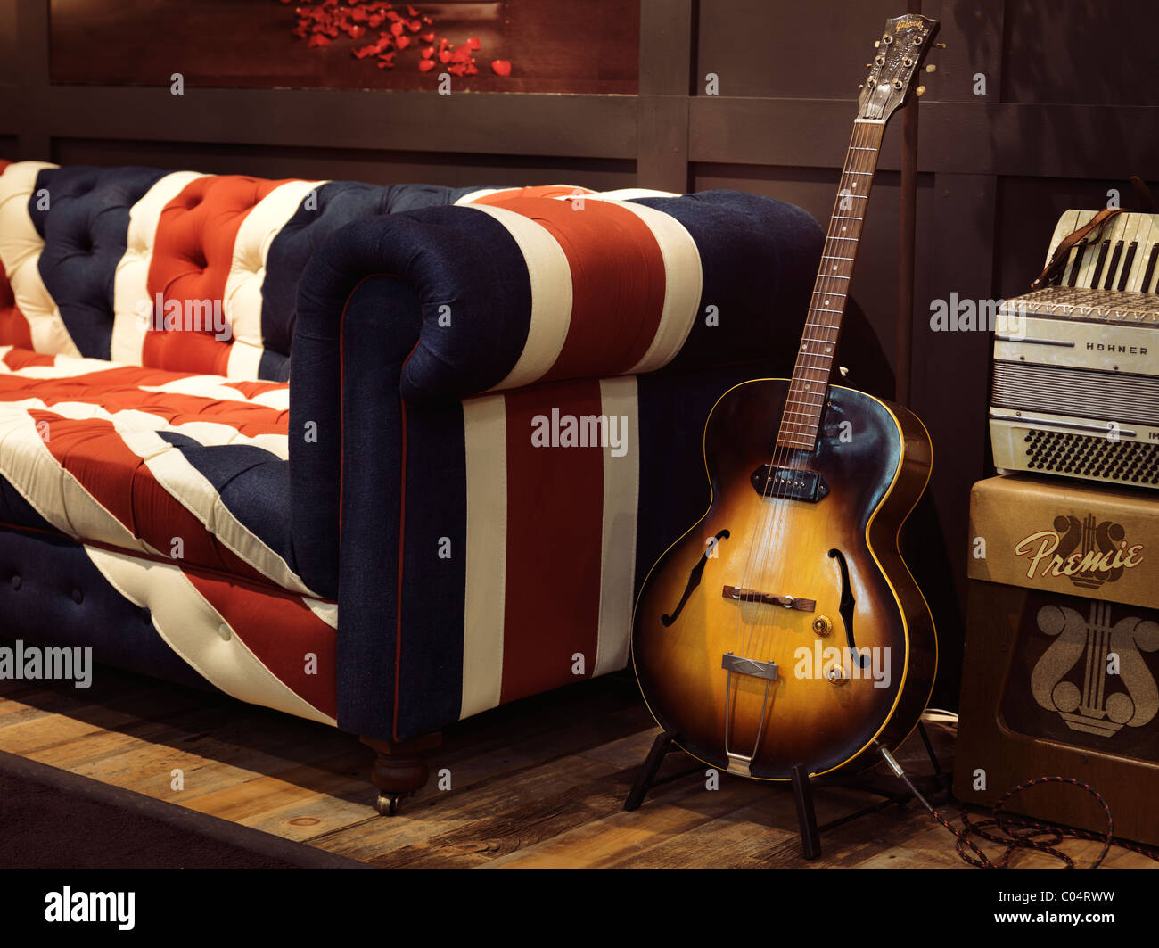 Vintage acoustic Gibson Guitar su un supporto a un divano con Unione Jack pattern su di esso Foto Stock